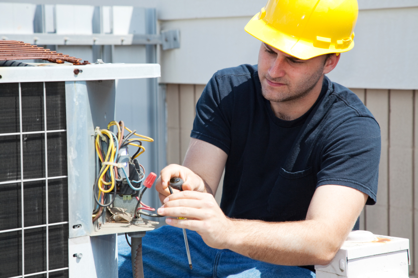 hoffman hvac technician repairing unit with yellow safety hat on outside near wires