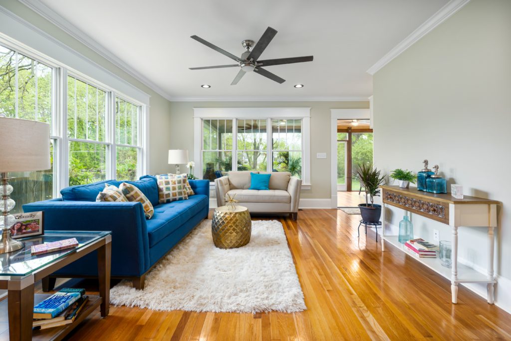 bright sunroom with blue furniture and a white rug with a 6 blade ceiling fan