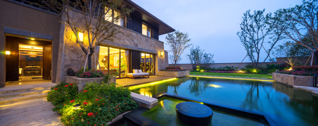 landscape lighting behind a lit home and pool